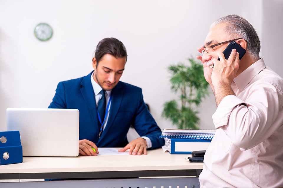 Pensionist telefoniert, Sachbearbeiter am Schreibtisch